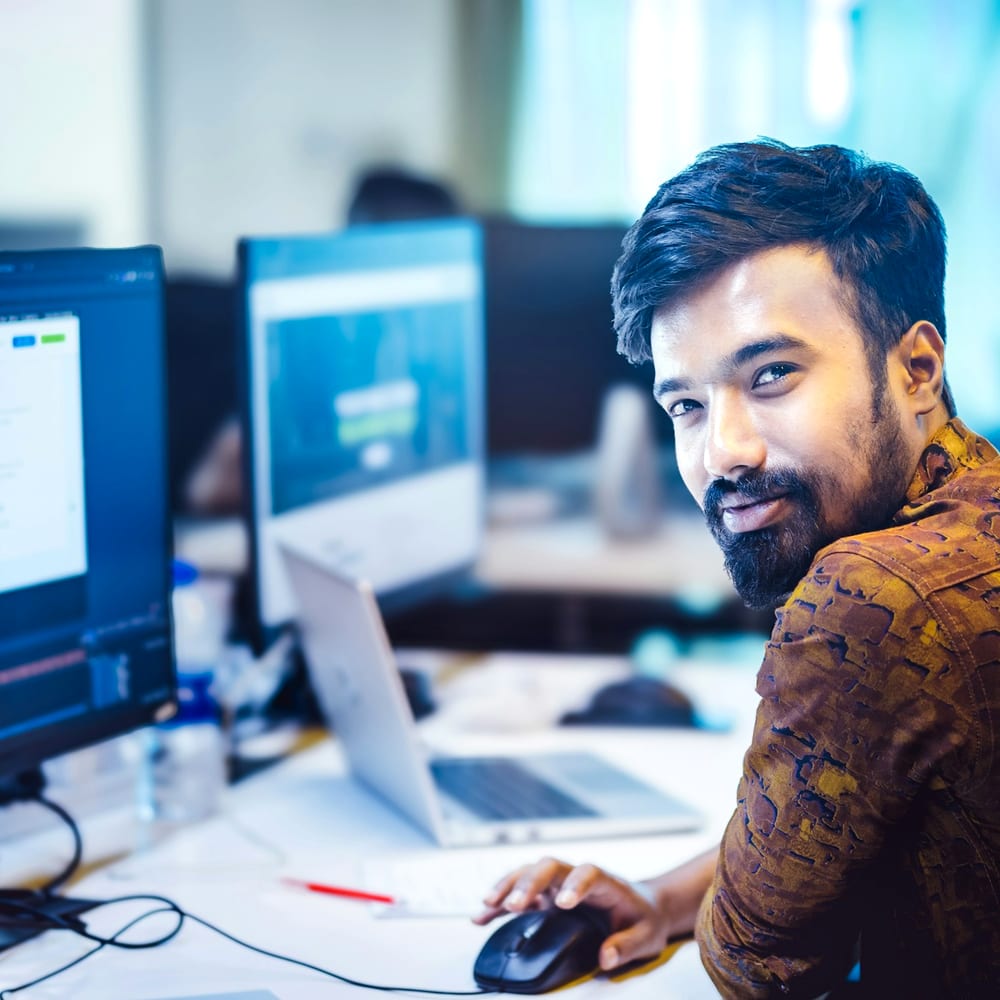 IT engineer managing cloud consoles across monitors and a laptop in an operations office